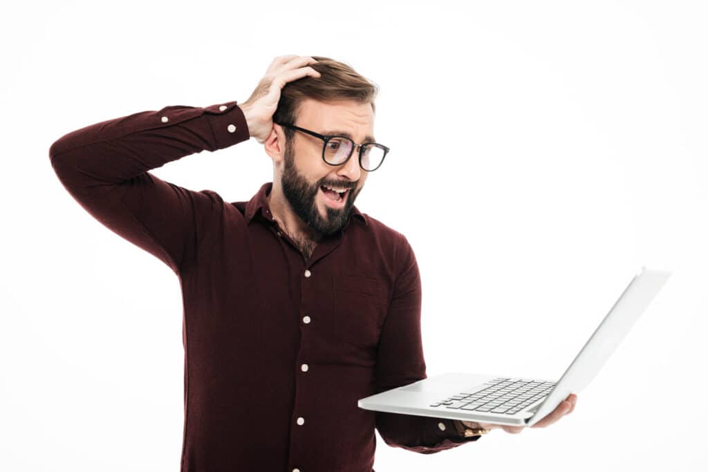 Portrait of a surprised young bearded man looking at laptop computer isolated over white background